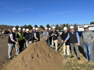 Cogmedix leadership wearing PPE, standing by a large pile of dirt and holding shovels, at the groundbreaking ceremony for the new medical engineering and manufacturing facility.