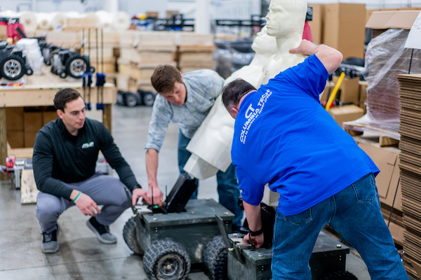 A Columbia Tech associate in a blue shirt helps two representatives from MVP Robotics assemble tactical training dummies