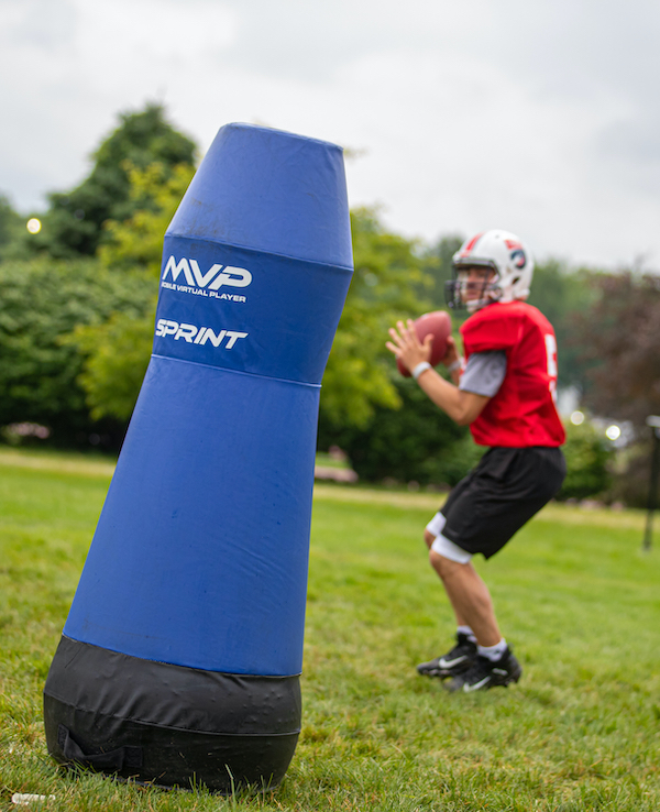 a blue tackling dummy stands in front of a football player in a red jersey