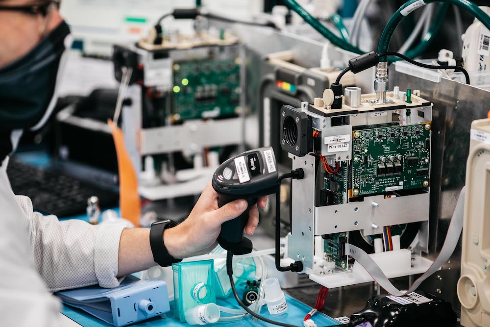 A caring associate at Cogmedix uses a hand-held scanner while working on a benchtop medical device.