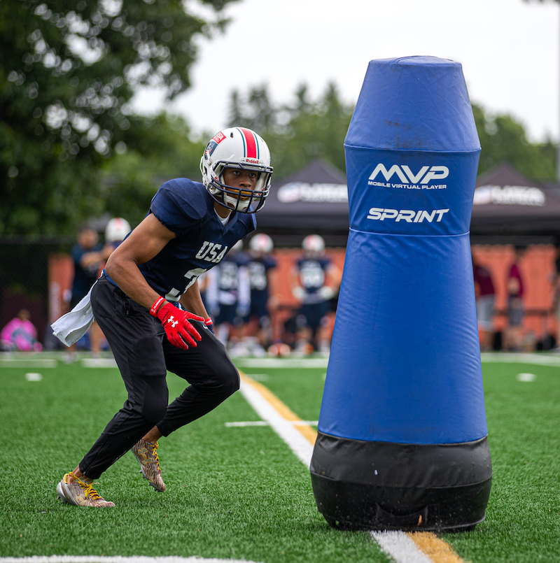 A football player runs toward a blue MVP Sprint football tackling dummy manufactured at Columbia Tech. 